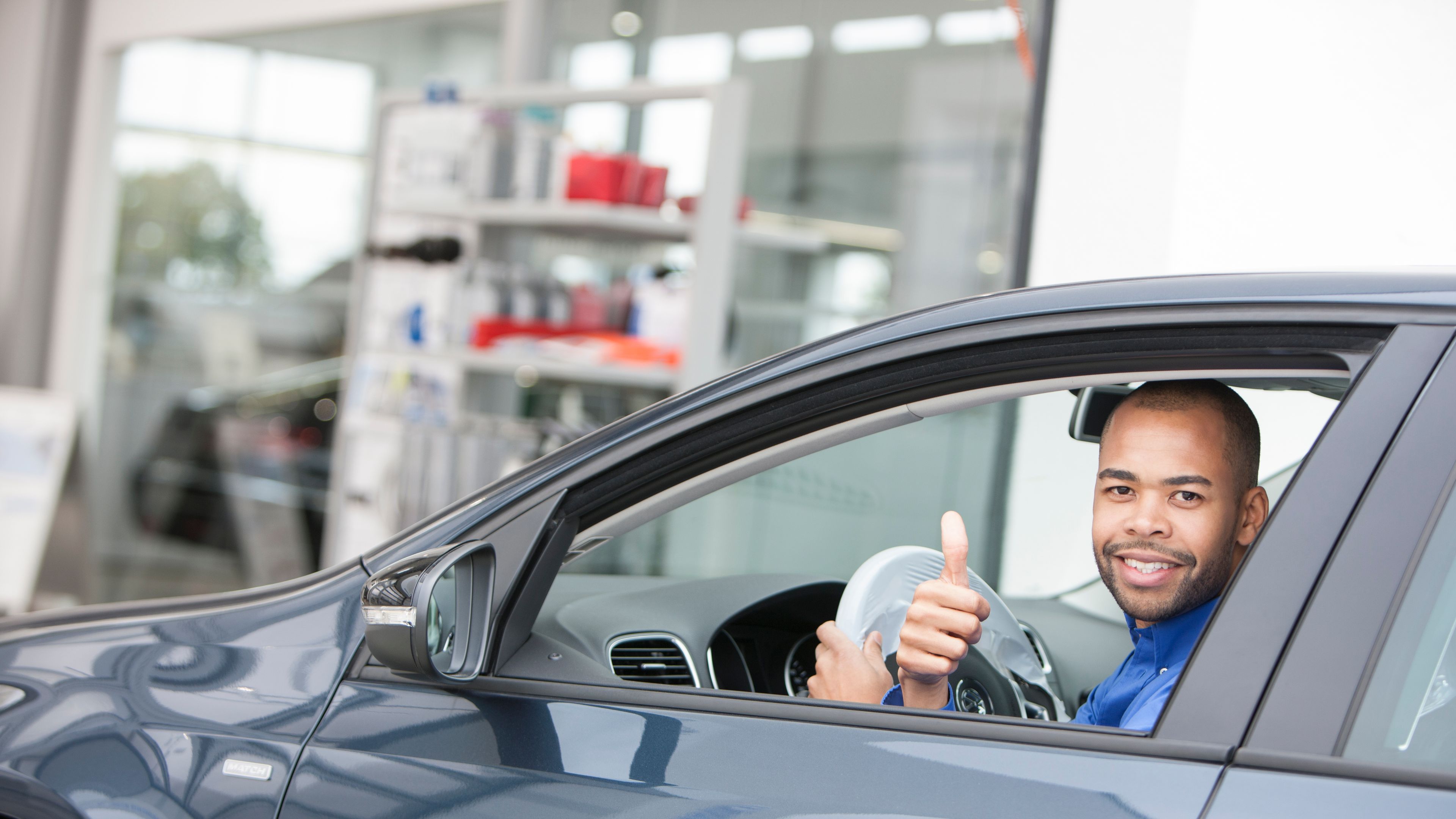 Ein Mann sitzt in einem VW und zeigt Daumenhoch aus dem Denster